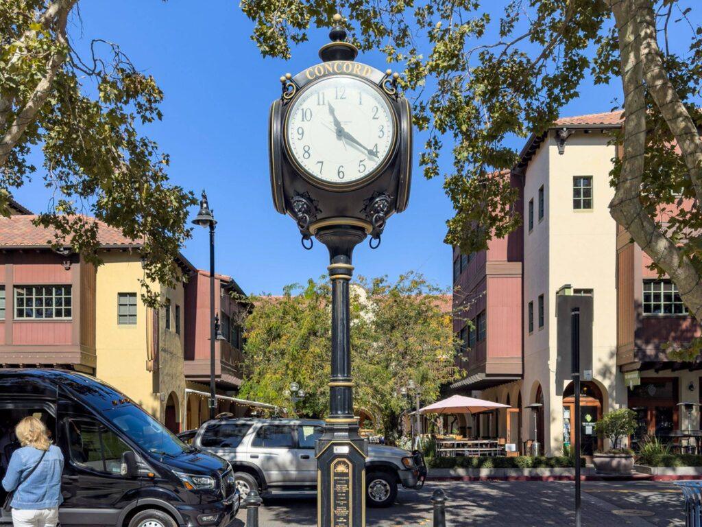 Historic Concord street clock in downtown Concord, California, surrounded by shops, trees, and outdoor dining along a sunny streetscape.