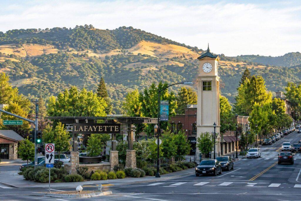 Downtown Lafayette, California streetscape featuring the Lafayette clock tower, scenic hills, tree-lined roads, and local traffic during daylight.