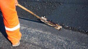 Paving contractor using a hand squeegee to spread black sealcoat emulsion during early fall asphalt maintenance